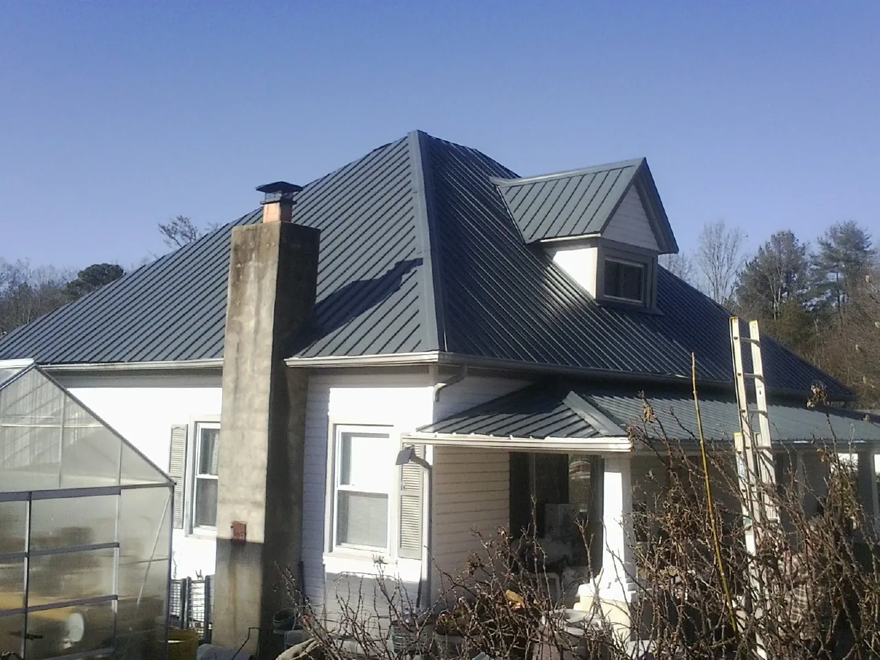 Dark blue standing seam metal roof on a white farmhouse with dormer — Slate & Tile Roof Repair by Roofing Brothers in Desmet