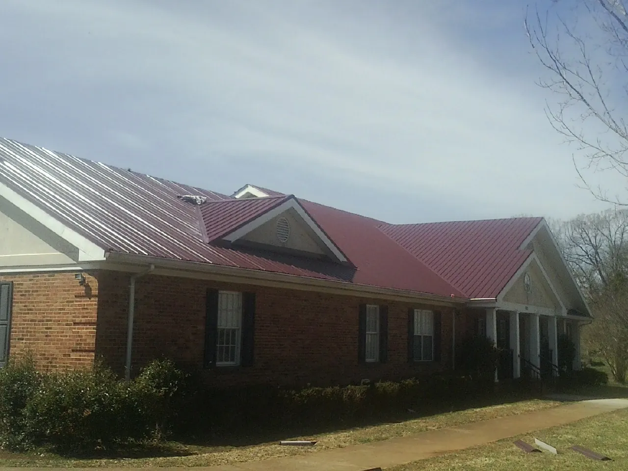 Red metal roof with gabled entries on a long brick building, from a Hail Damage Roof Repair job in Desmet