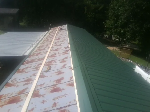 Old rusted panels beside newly installed green metal roofing — Wind Damage Roof Repair by Roofing Brothers in Desmet