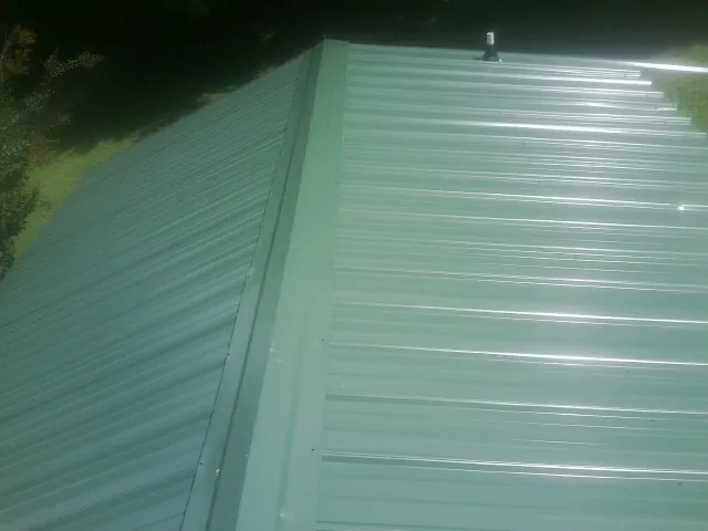 New green metal panels meeting at the ridge of a roof — Flat Roof Repair work by our crew in Desmet