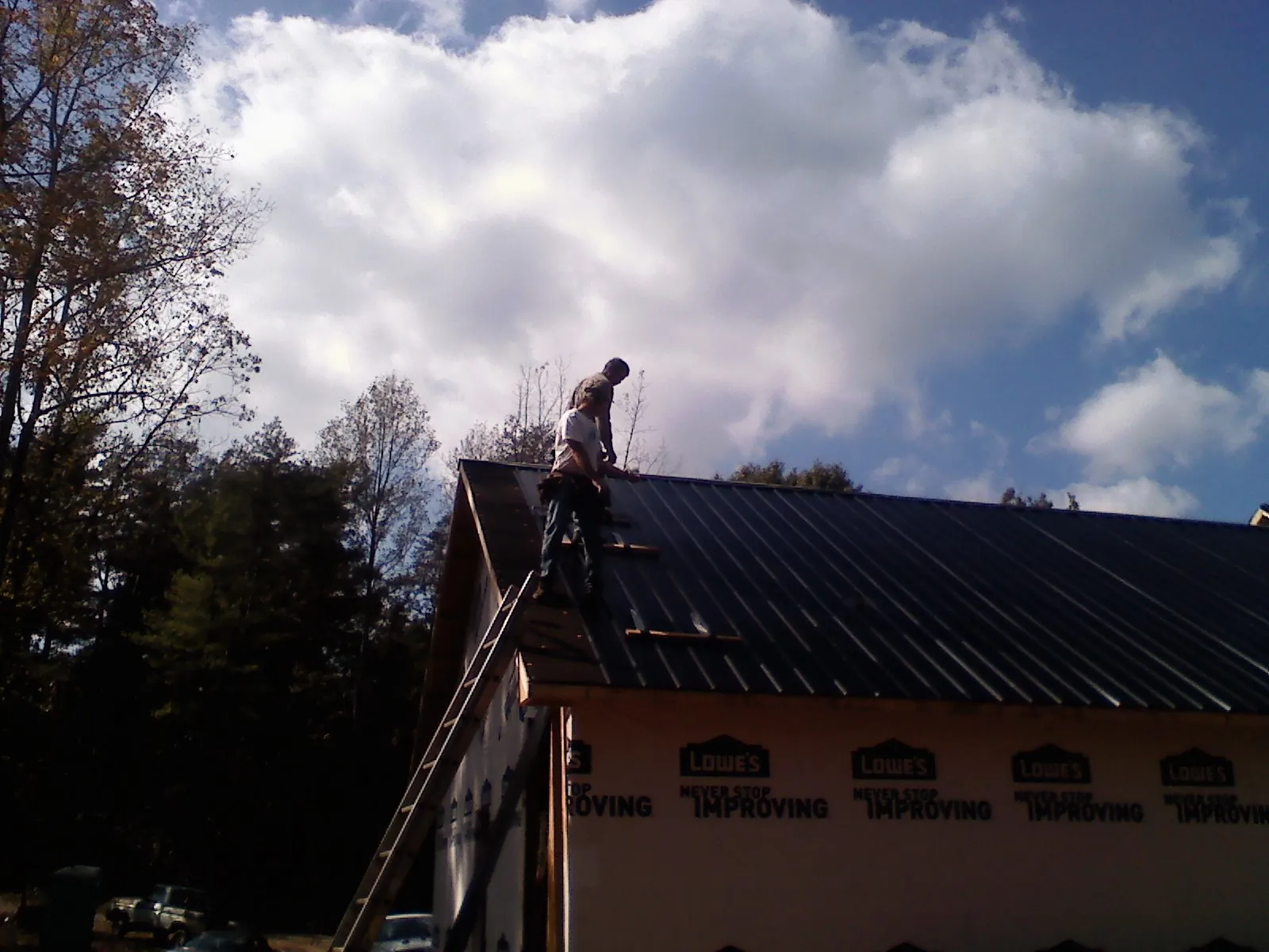 Roofer fastening dark metal panels high against a cloudy sky, from a Roof Inspection job in Desmet