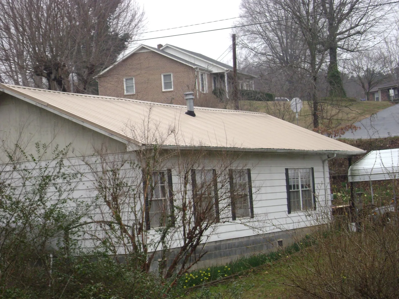 Tan metal roof on a white sided house set into a hillside — Commercial Roofing by Roofing Brothers in Desmet