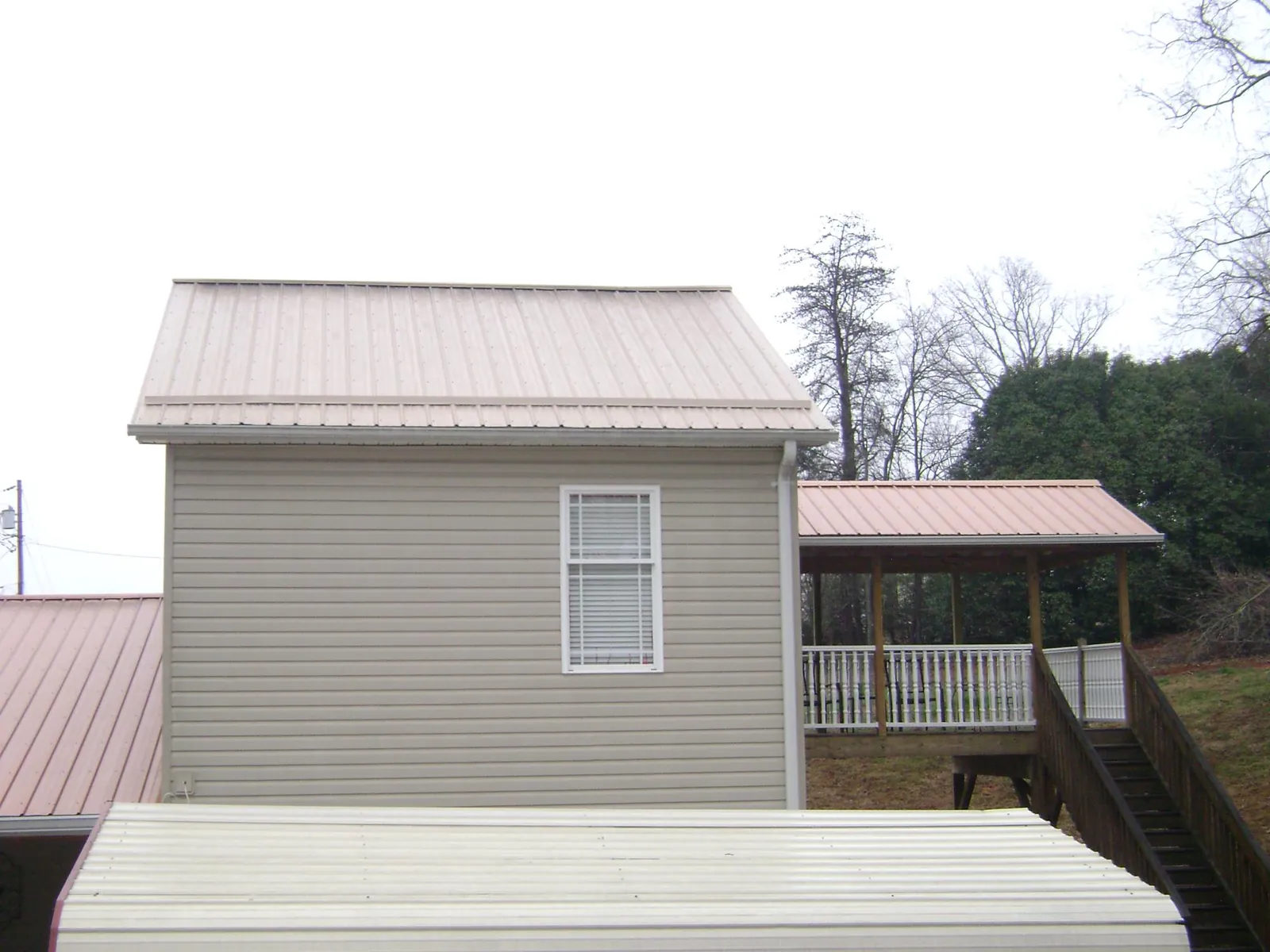 Tan metal roofs on a two story addition and attached porch, from a Roof Replacement job in Desmet